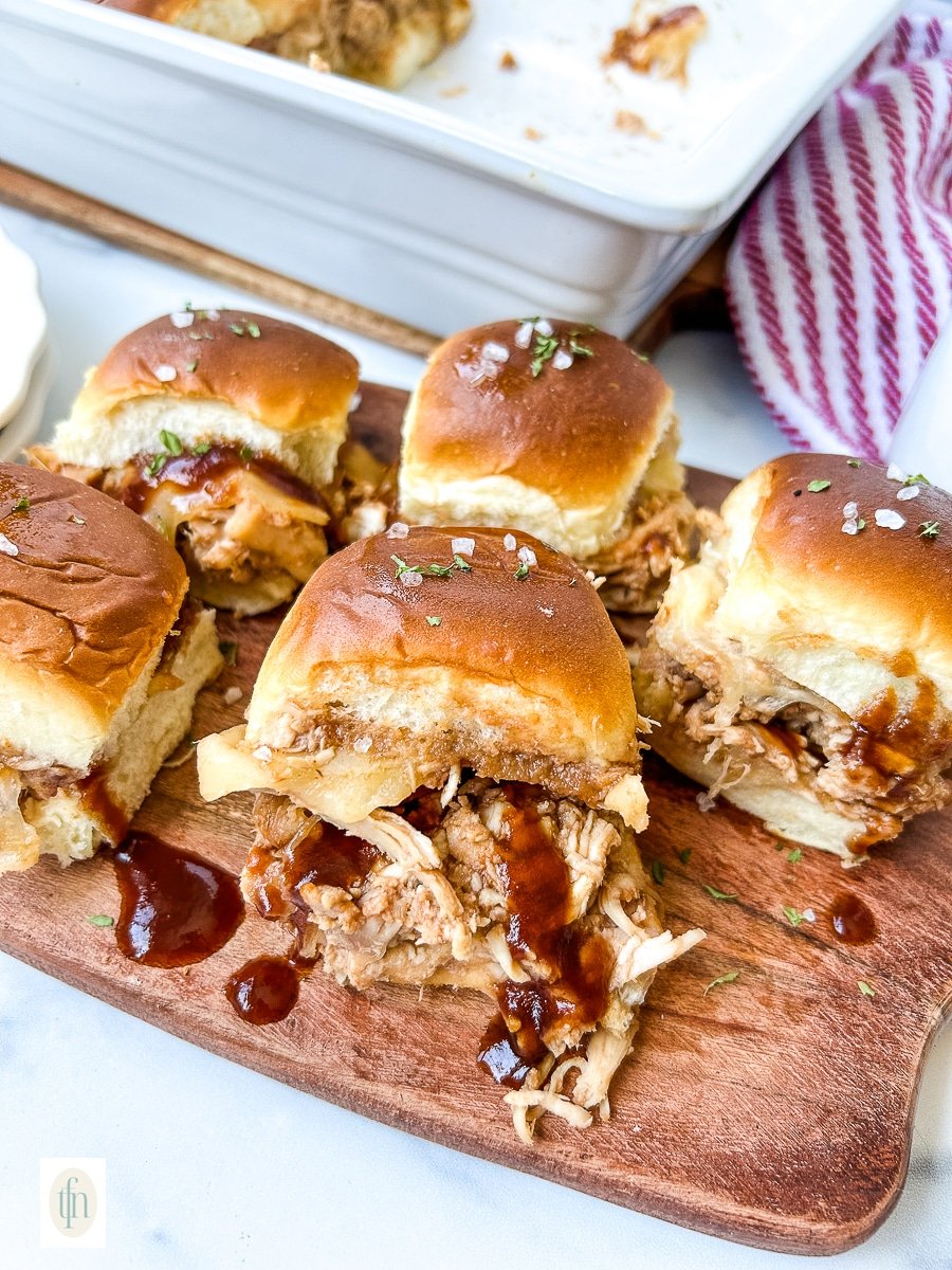 Wooden serving platter filled with shredded BBQ chicken sliders for game day party.
