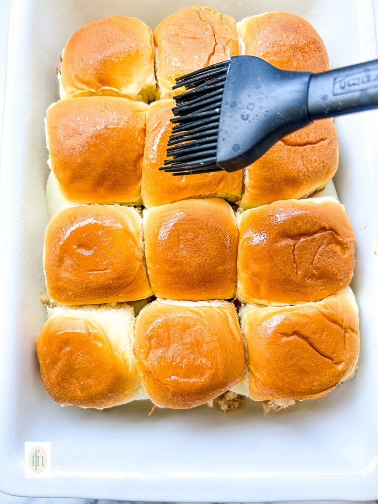 Brushing the tops of small buns with melted butter.