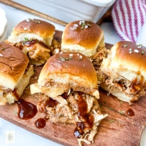 Five BBQ chicken slider sandwiches on a wood serving board.