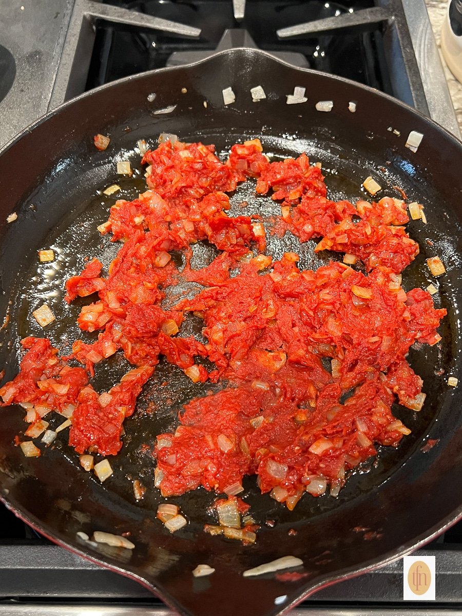 Cooking tomato paste with onions and garlic in a cast iron skillet.