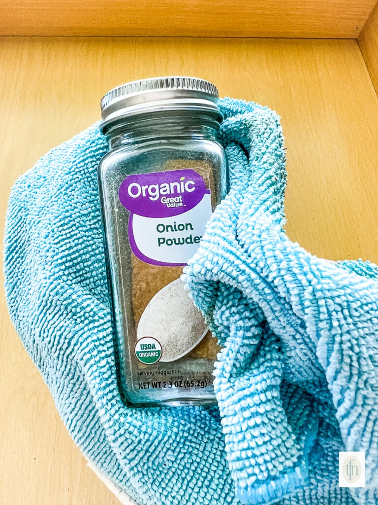 Cleaning a glass jar of onion powder with a blue microfiber cloth.