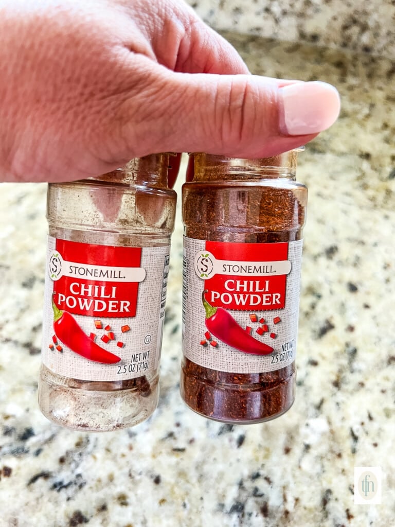 Organizing a spice drawer by combining two bottles of chili powder.