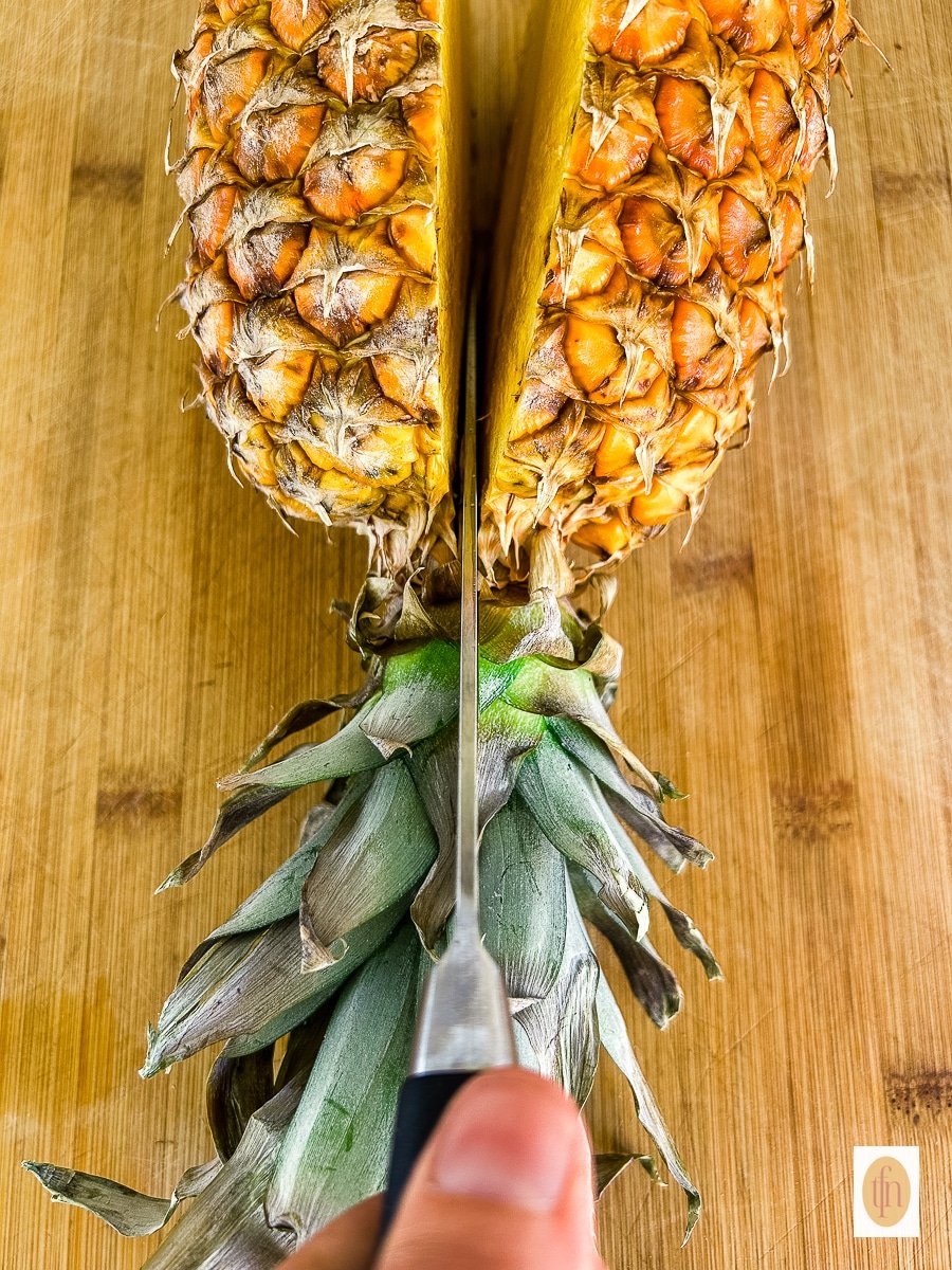 Using a large knife to cut a pineapple in half for bowls.