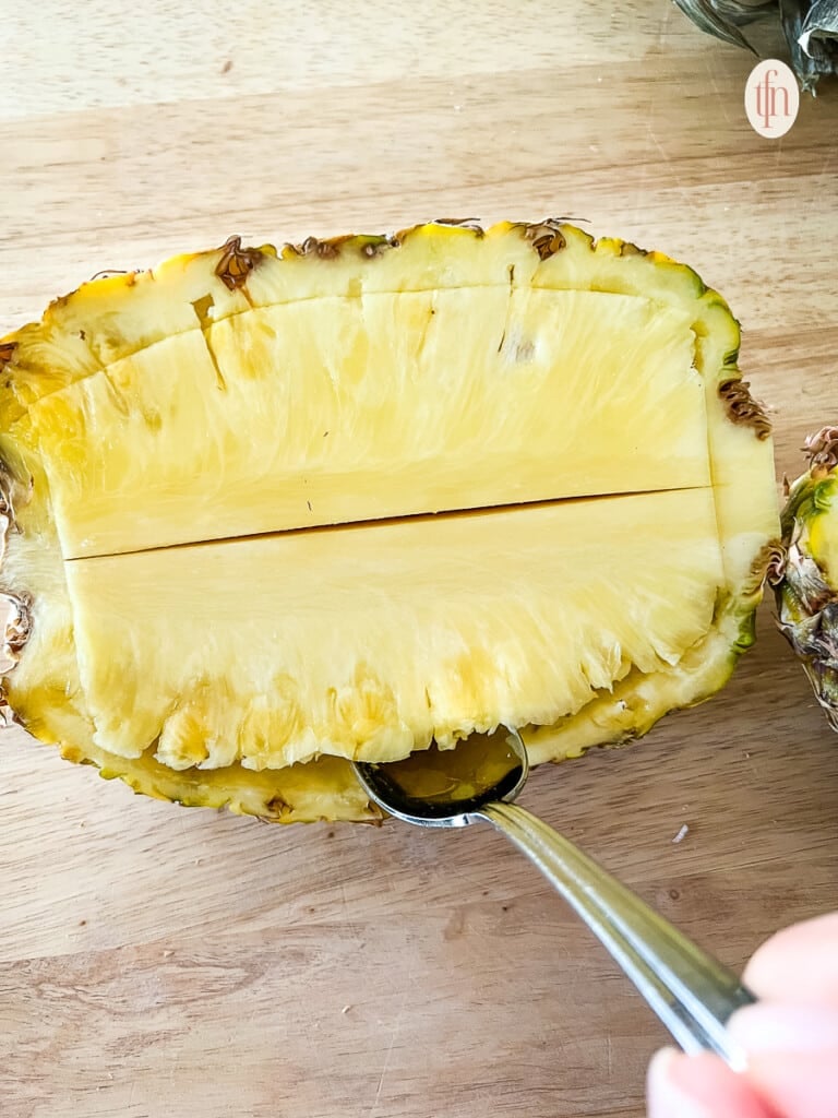 Using a spoon to remove the fruit and core from a pineapple.