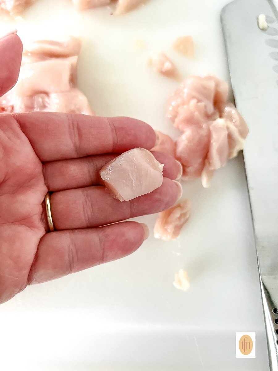 Chicken breast cut into cubes in a woman's hand, shown close up.