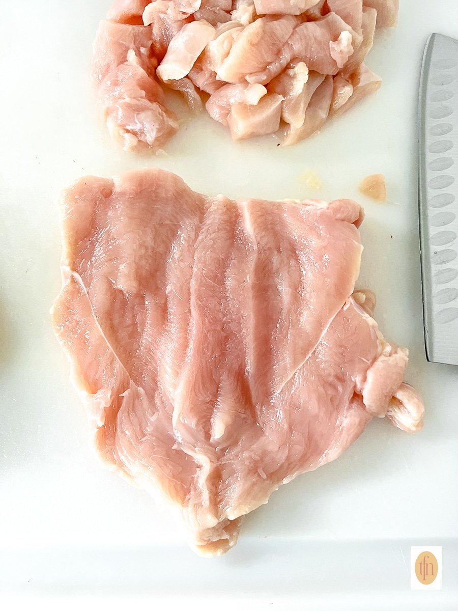 Butterflied piece of raw poultry on a white cutting board.