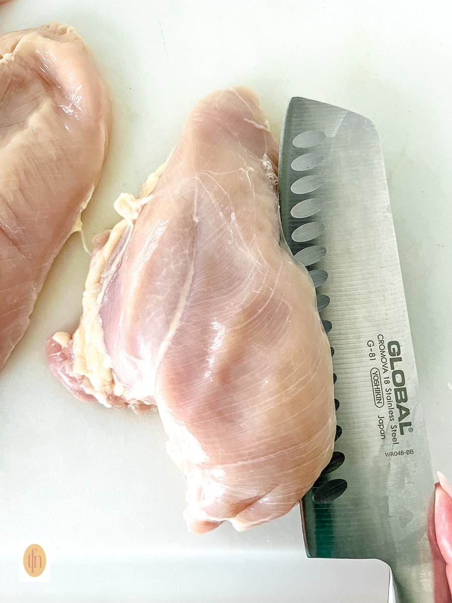 a chef's knife cutting boneless breast into two cutlets.