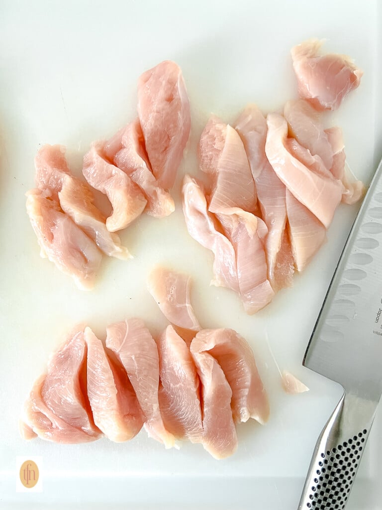 Chicken breast cut into strips on a cutting board.