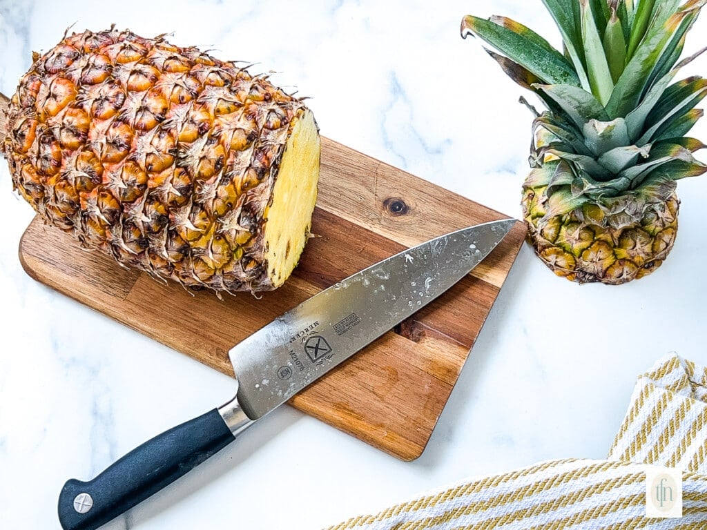 Top crown cut off of a whole pineapple, sitting next to the remaining fruit.