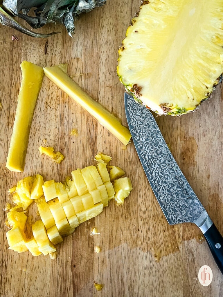 Chopped tropical fruit on a cutting board next to a large Shun chef's knife.