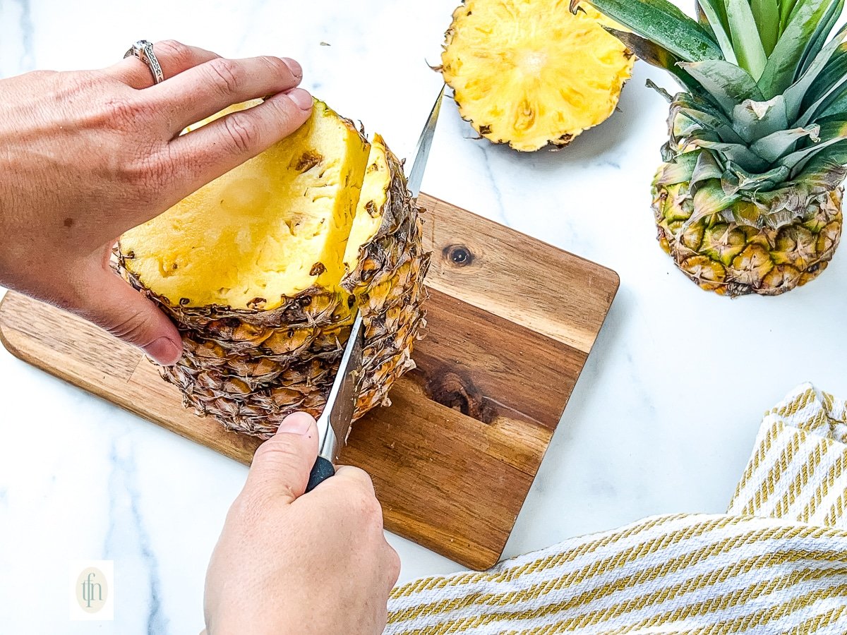 Using a large kitchen knife to show how to peel a pineapple.