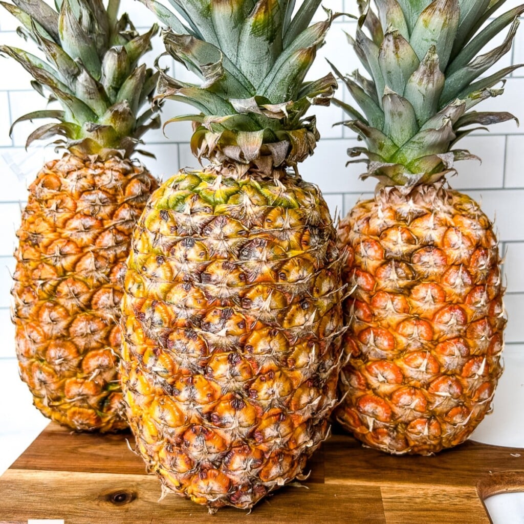 3 whole pineapples on a cutting board.