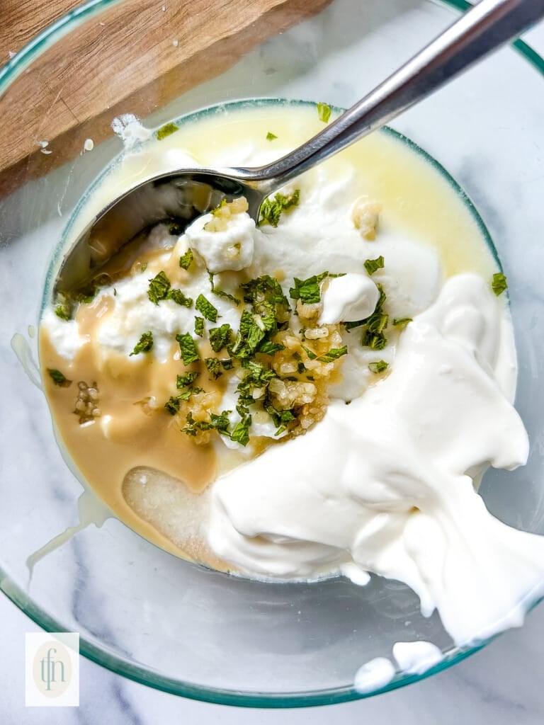 Using a spoon to combine shawarma sauce ingredients in a small bowl.