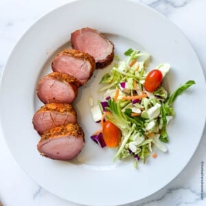 Slices of smoked pork tenderloin on a white dinner plate with a side salad.