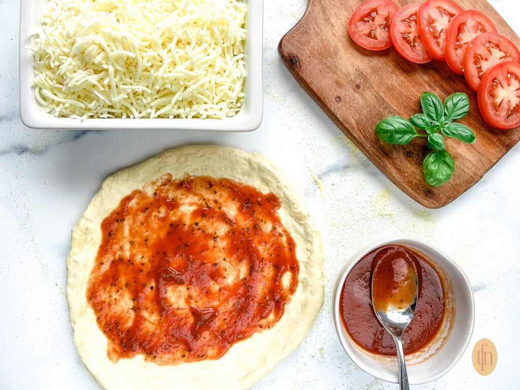 Assembling sourdough pizza crust with toppings and cheese.