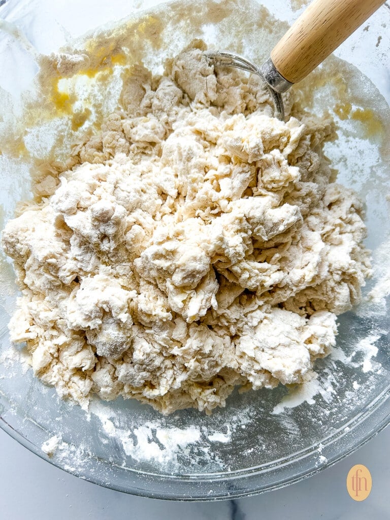 Shaggy looking mixture of water and flour combined together with a whisk in a mixing bowl.