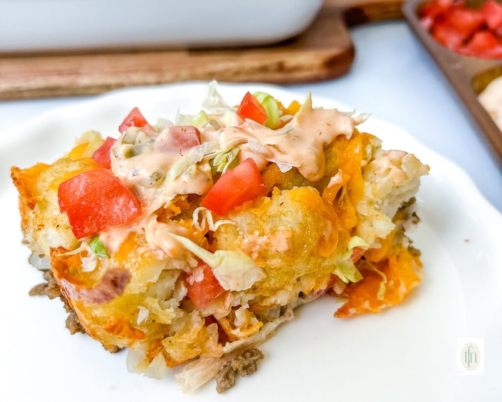 Close up of baked comfort food meal of ground beef, potatoes, cheese, tomatoes and shredded lettuce.