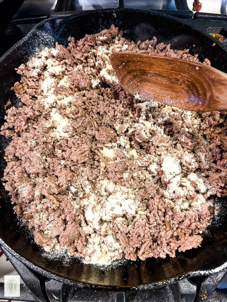 Browning ground beef with onion and garlic powder in a cast iron skillet.
