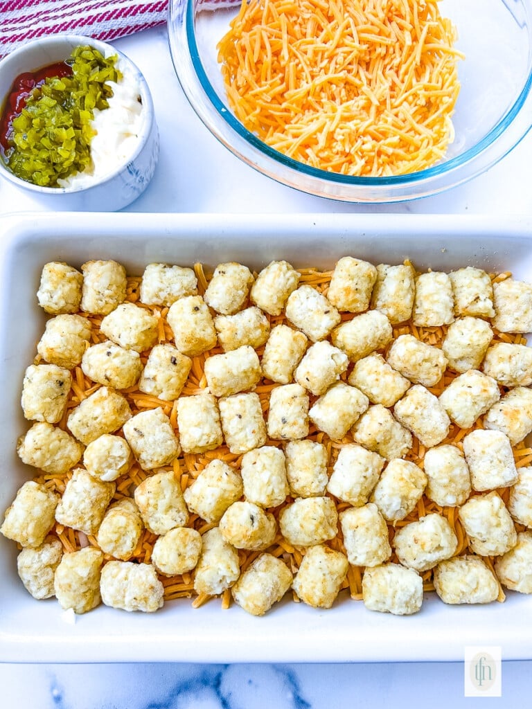 Layer of frozen potato tots on top of a cheeseburger casserole.