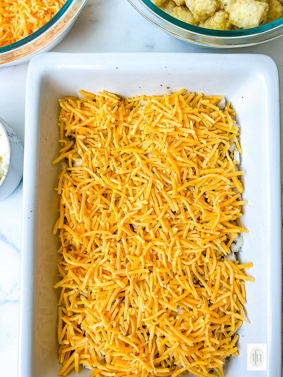 Shredded cheddar cheese layered into a baking dish.