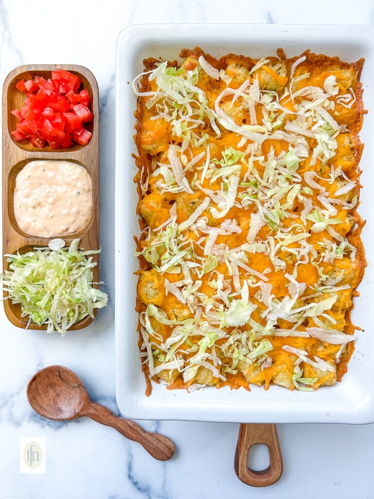 hamburger potato casserole topped with shredded lettuce next to a dish with diced tomatoes and Big Mac sauce.