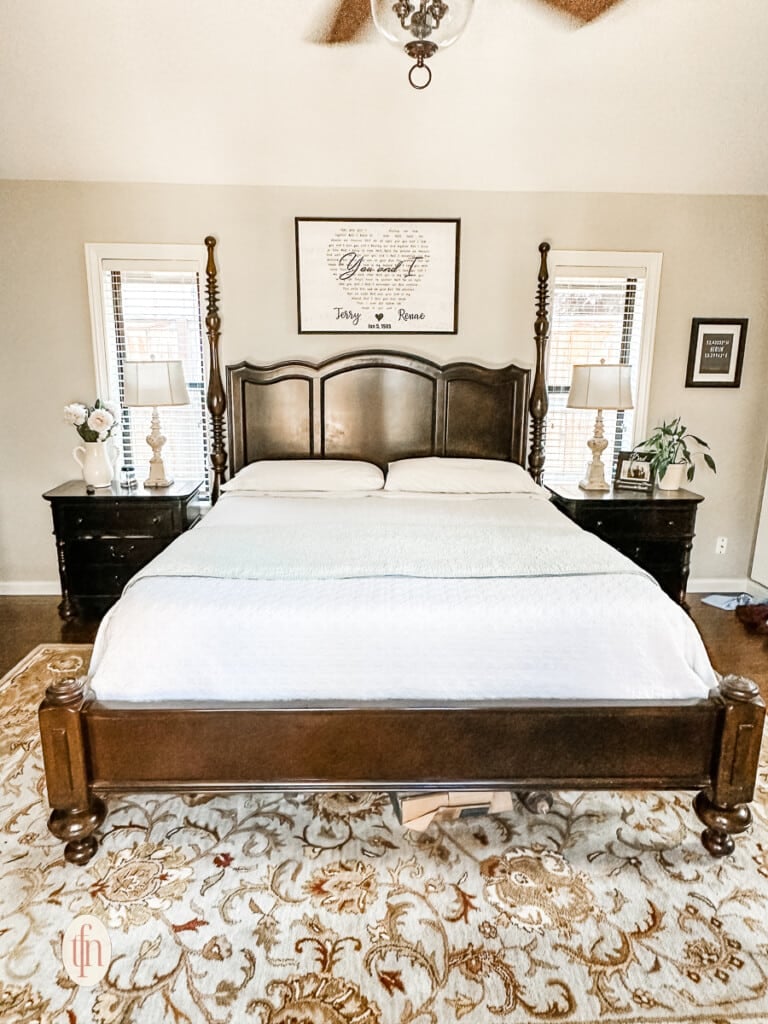 Partially unmade bed in a large bedroom with nightstands, lamps, and accent carpet over wood flooring.