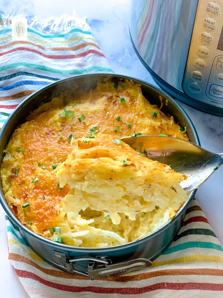 Scoopful of cheesy hashbrowns on a large serving spoon.