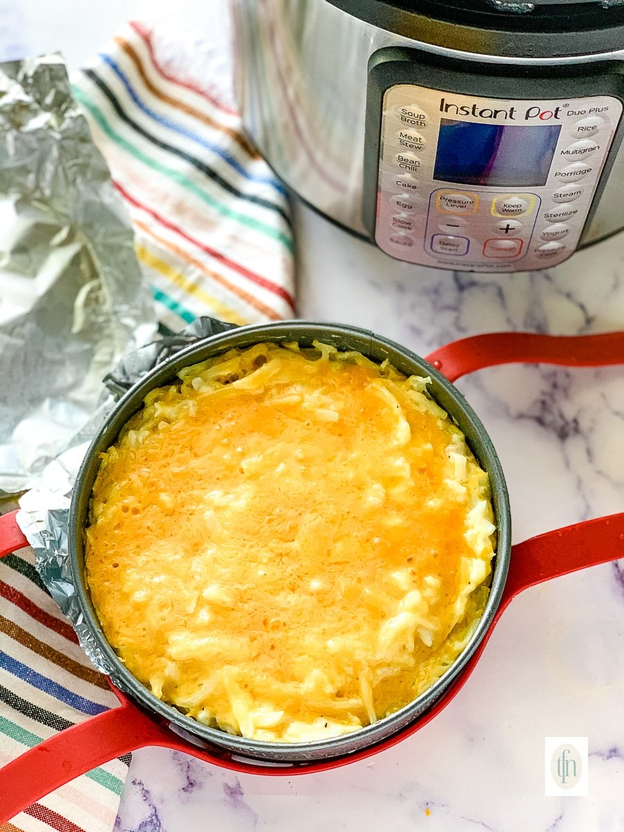 Hashbrown casserole in a small round pan sitting next to a pressure cooker.