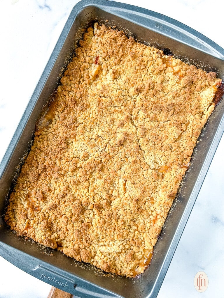 Baked peach dessert with crumble topping in an regtangular baking pan.