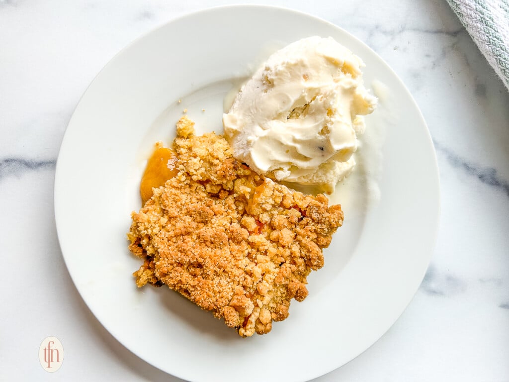 Serving of cake mix peach cobbler topped with vanilla ice cream.