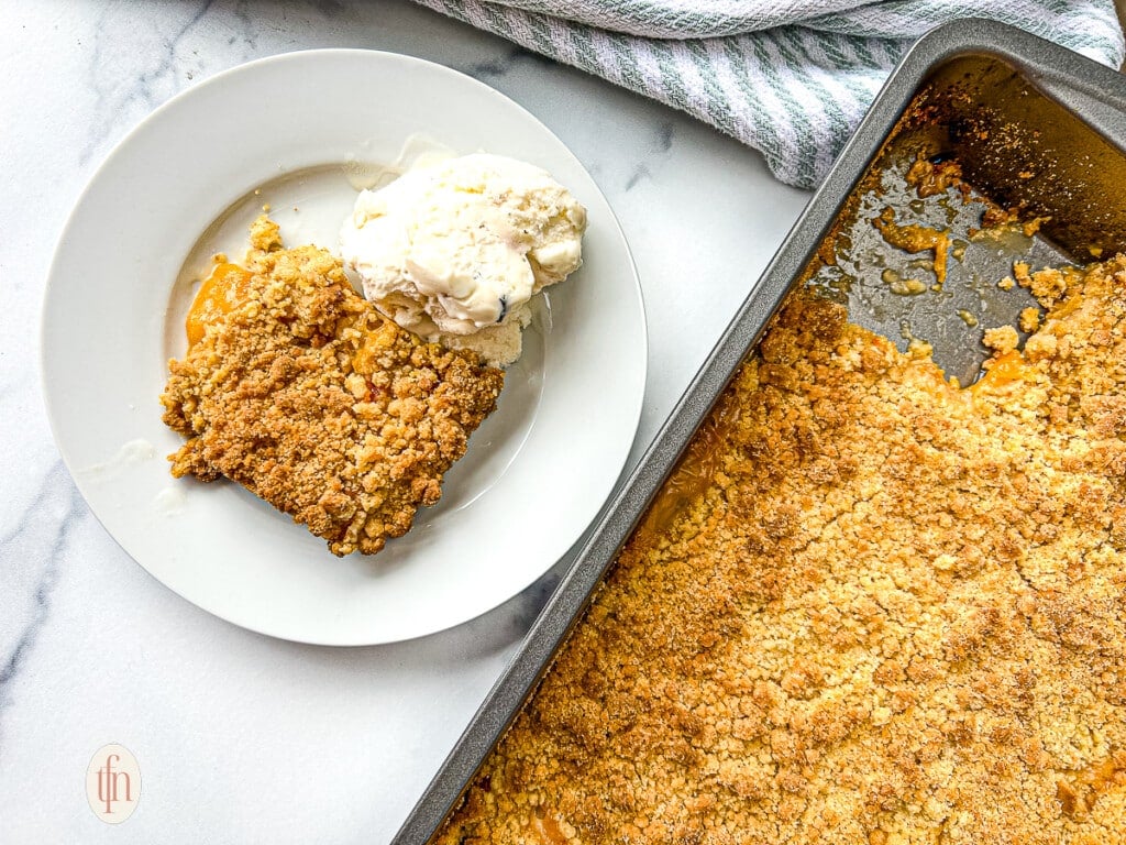 Baked dessert with peaches in a pan, and sliced serving on a small white plate.