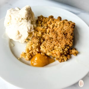 A plated serving of cobbler with peaches and a scoop of vanilla ice cream.