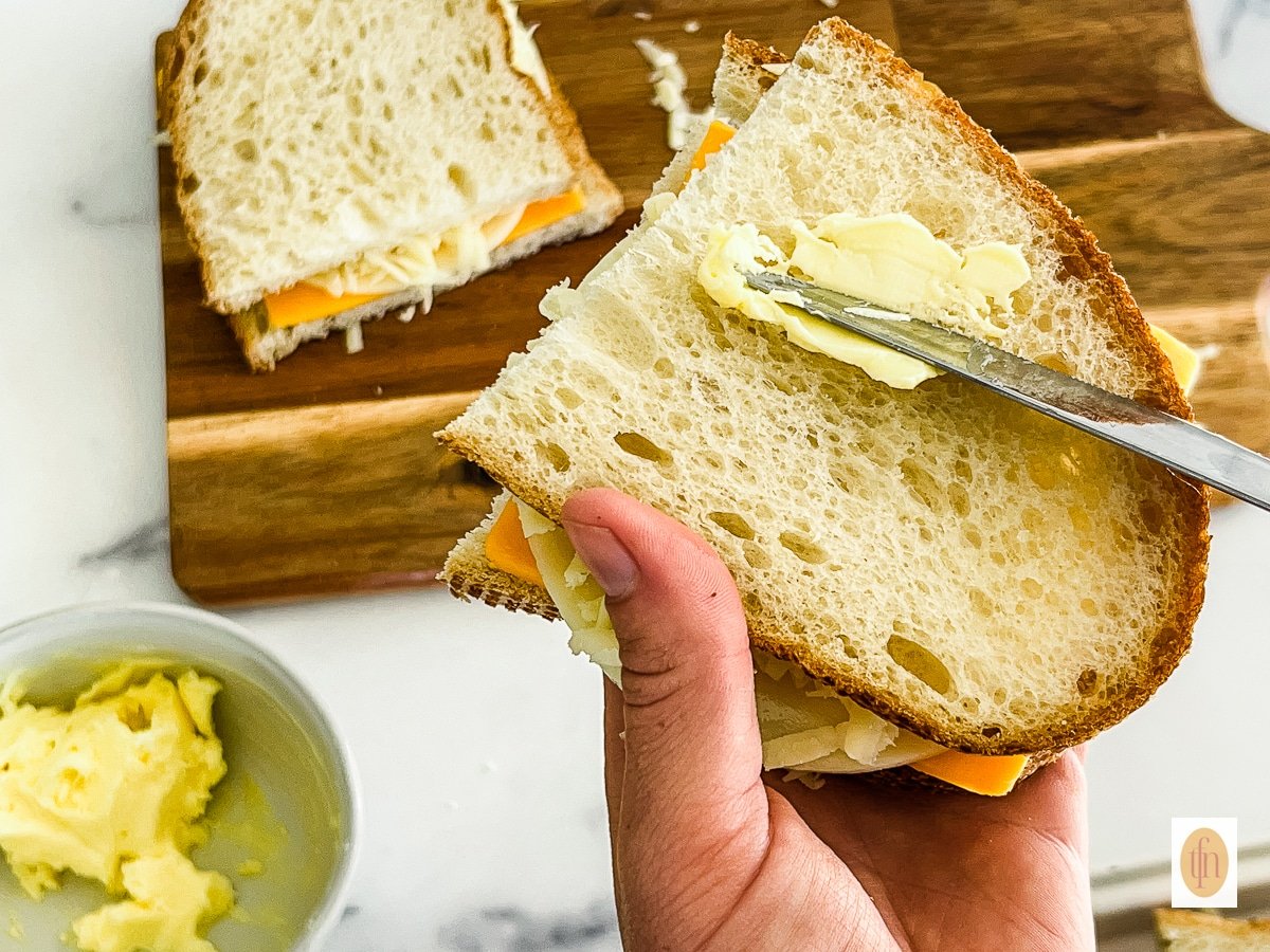 Buttering a sourdough bread sandwich before cooking on griddle.