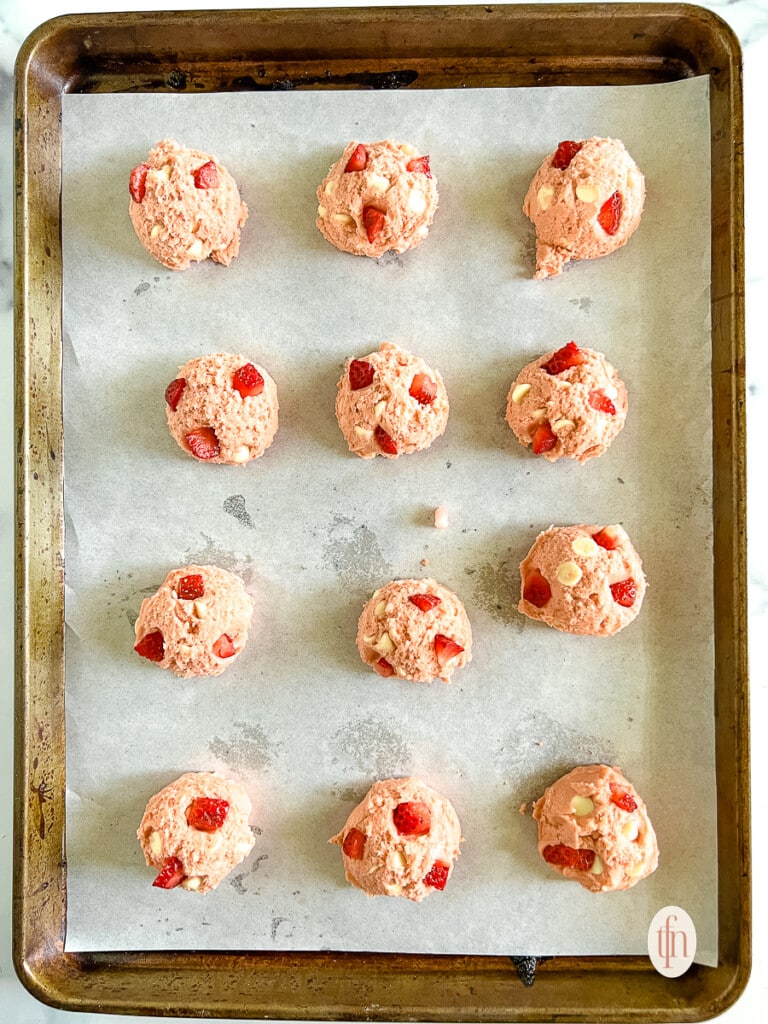 Unbaked strawberry cheesecake cookies arranged on a rimmed baking sheet lined with parchment paper.