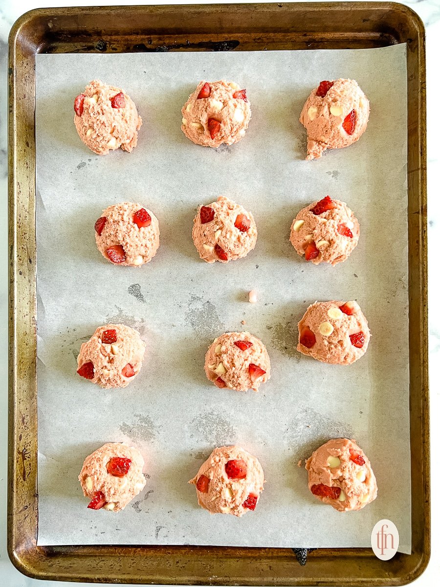 Unbaked strawberry cheesecake cookies arranged on a rimmed baking sheet lined with parchment paper.