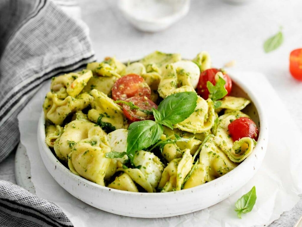 Perfectly tender cheese-filled pasta, cherry tomatoes, and mozzarella balls, all covered with green sauce in a white pasta bowl.