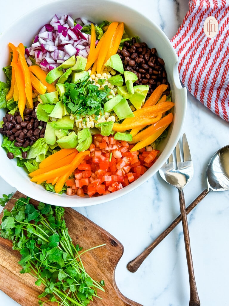 Tex Mex salad with avocado, bell peppers, corn kernels, red onion, cilantro, black beans, and diced tomatoes.