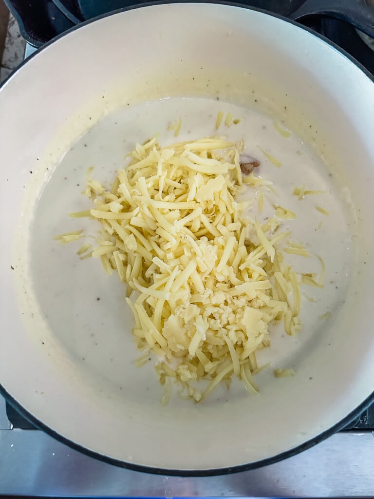 Shredded white cheese in a pot of bechamel sauce.