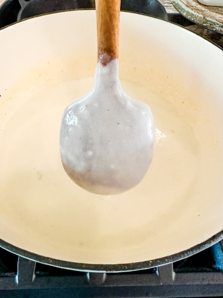 White mac and cheese sauce coating the back of a wooden spoon.