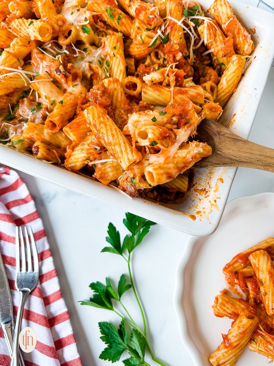 Wooden spoon in a dish of baked rigatoni with sausage.