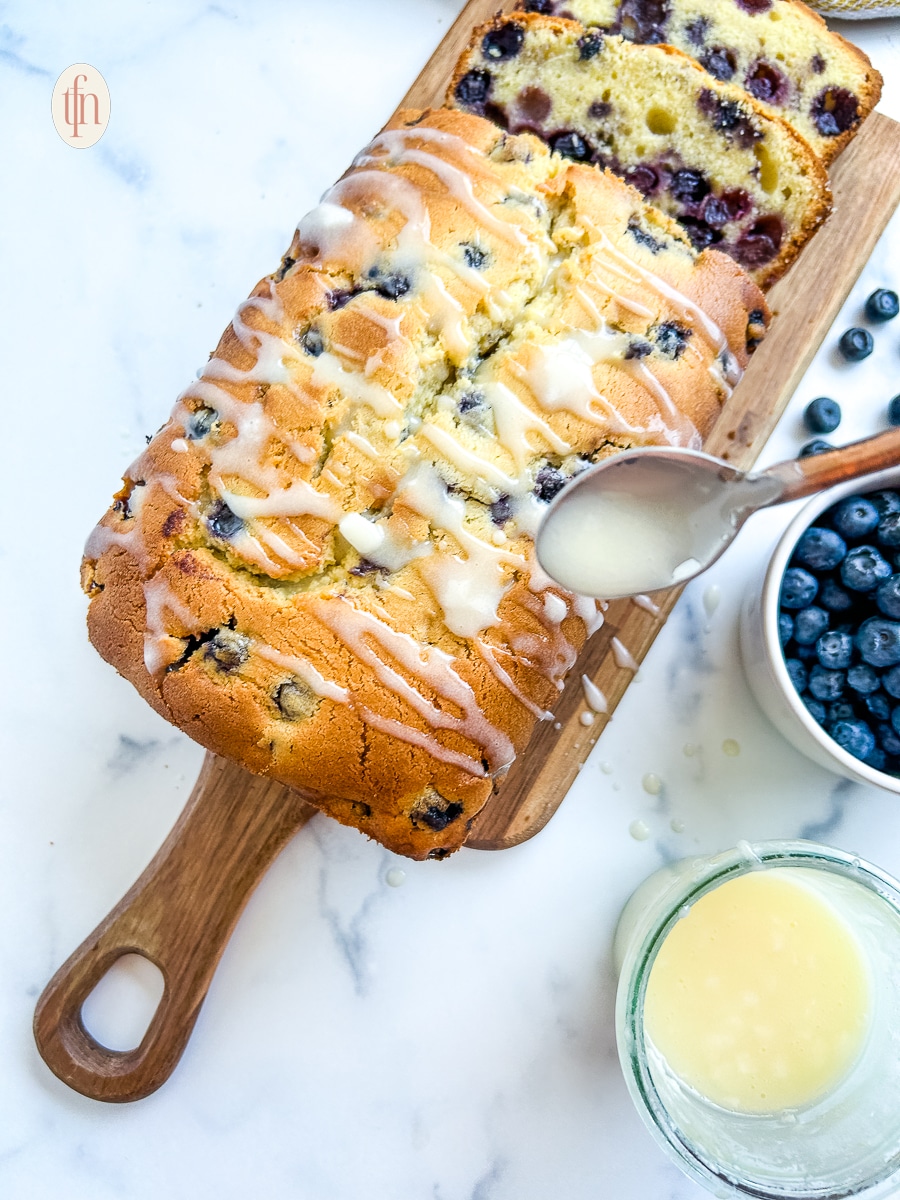 Using a spoon to drizzle glaze over a blueberry pound cake.