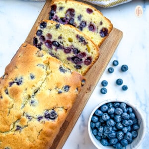 Blueberry pound cake on a cutting board next to a bowl of fresh blueberries.
