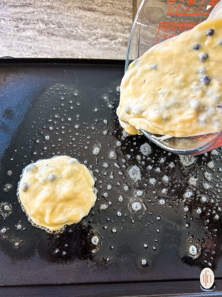 Pouring batter onto a hot buttered griddle.