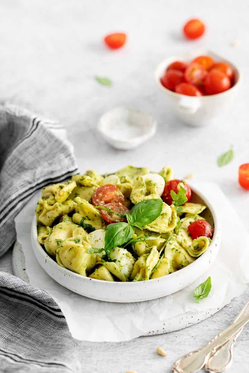 Plated serving of summer pasta dish with caprese ingredients of tomato, mozzarella pearls, and fresh basil.