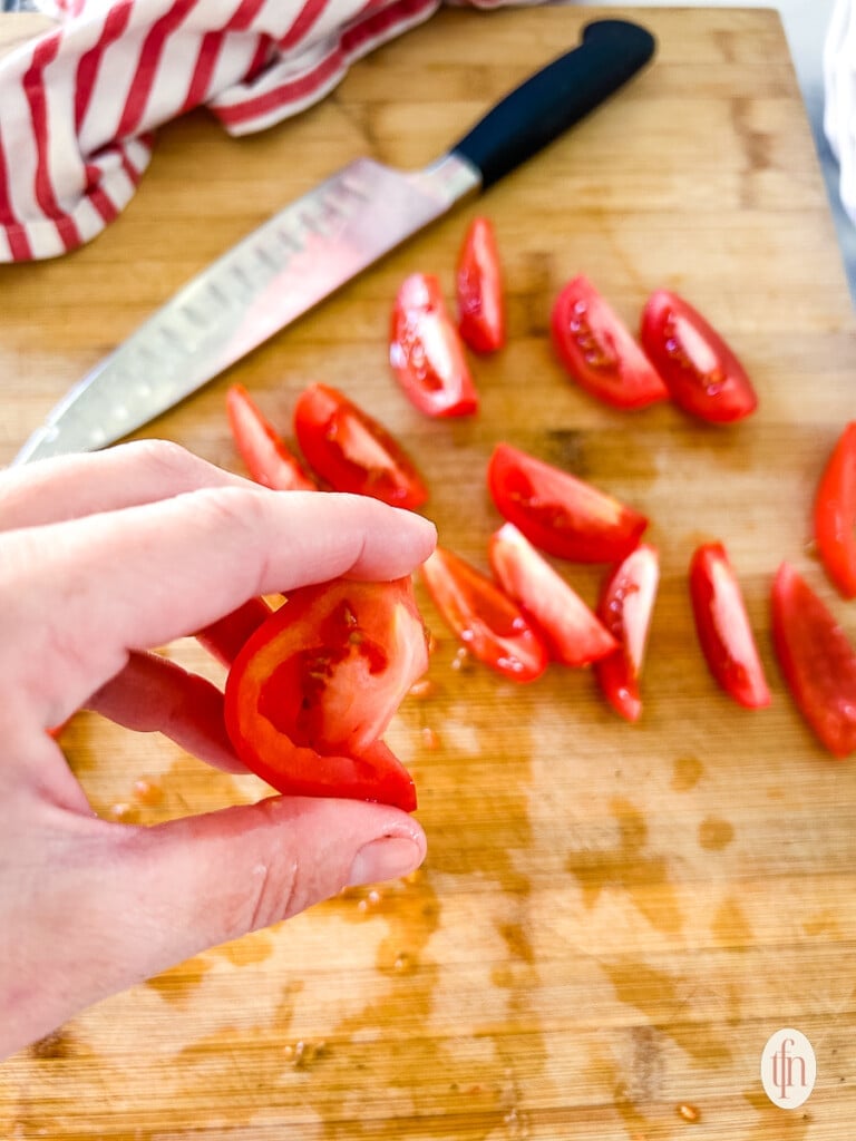 Gently squeezing chopped Roma tomatoes to remove juices.