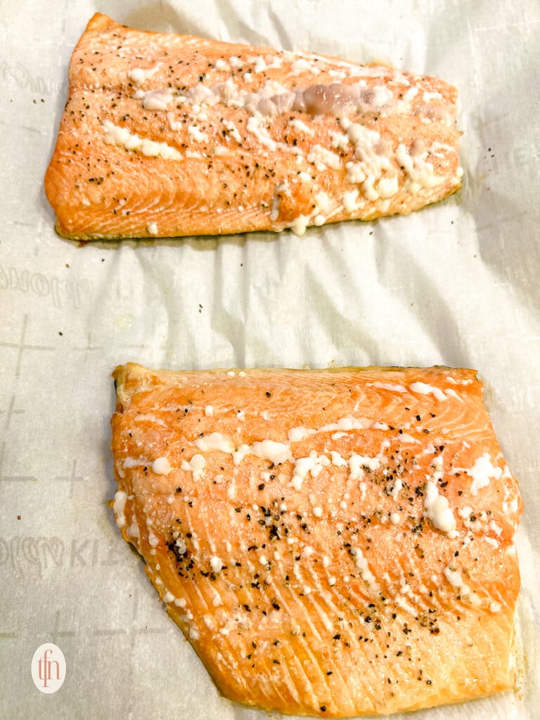 Two filets of baked fish on parchment paper lined baking sheet.