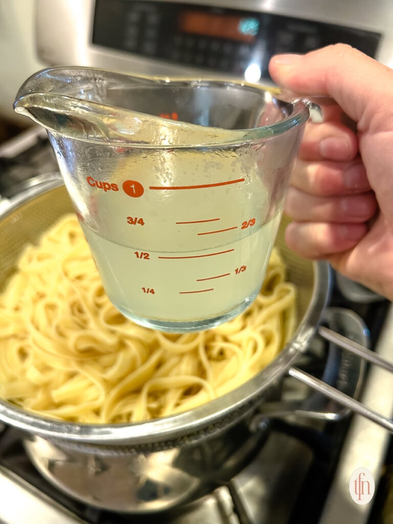 Woman's hand holding a glass measuring cup filled with pasta cooking water.