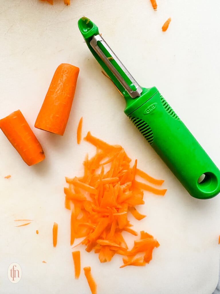 small pieces of raw orange vegetable next to a green colored vegetable peeler.