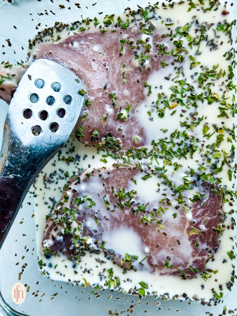 Tenderizing two uncooked pork chops in brine.