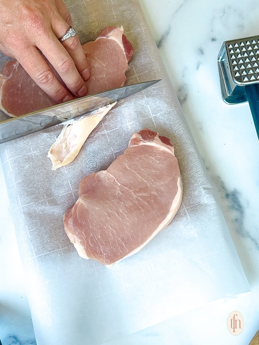 Trimming excess fat from a piece of raw meat.